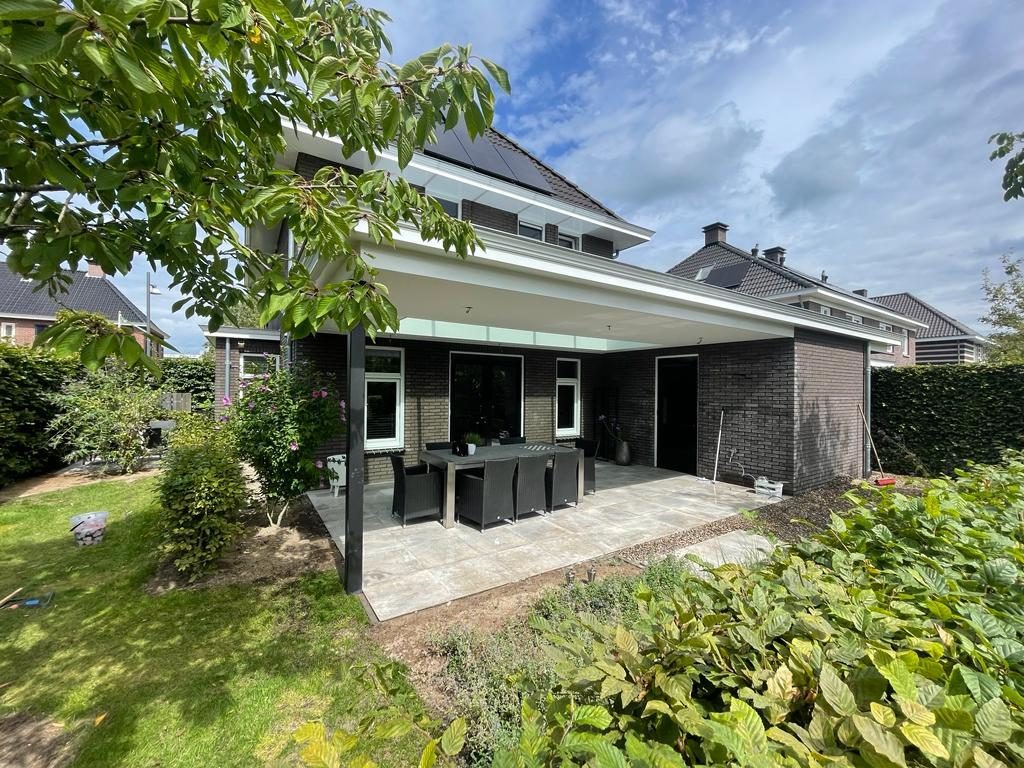 Moderne achtertuin met veranda, gazon en bloeiende borders